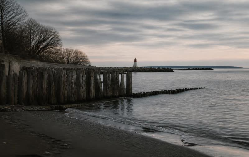 Low morning light on the Lake Ontario shoreline, with wet rock in the foreground and open water beyond.